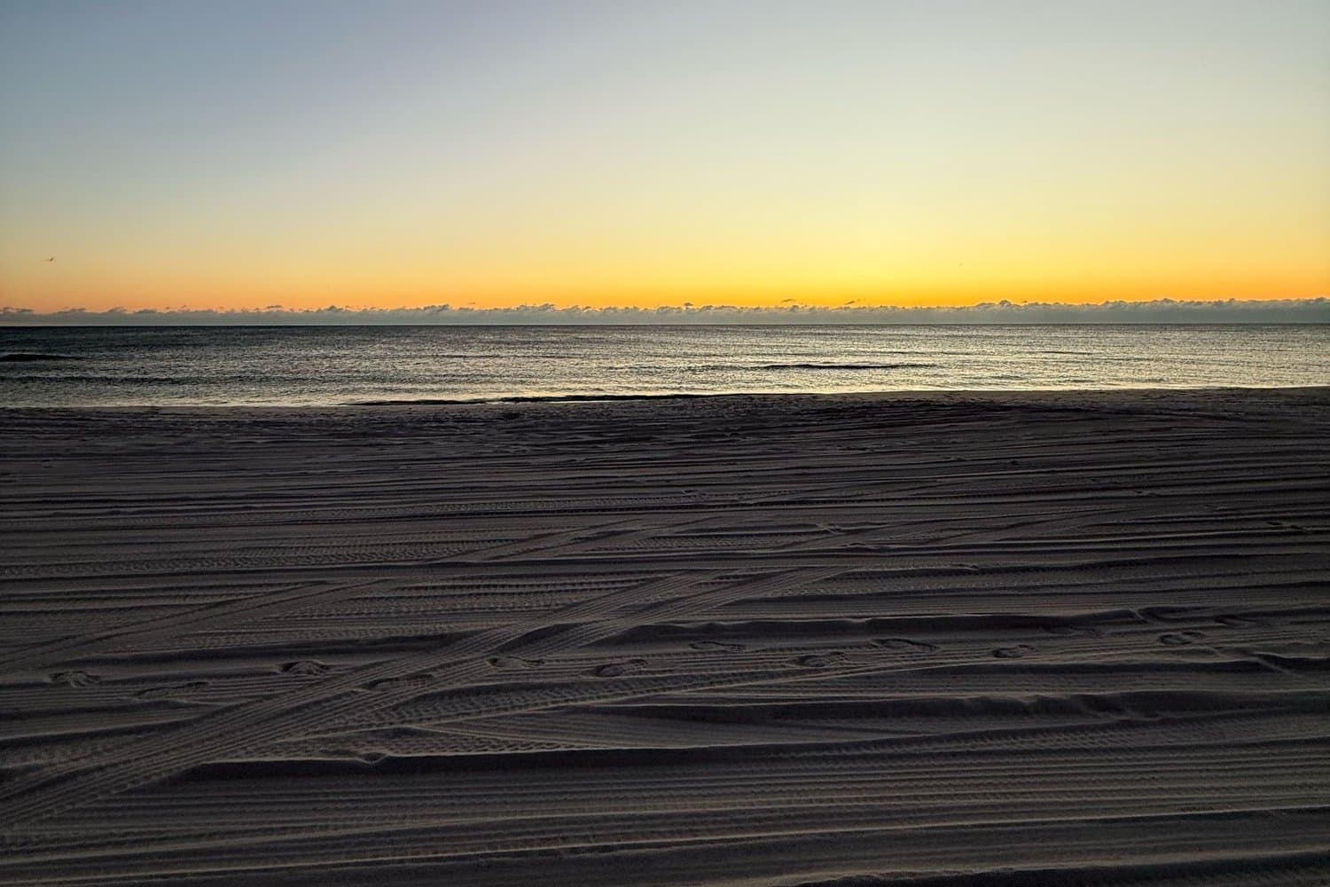 Tire tracks on the beach at sunrise